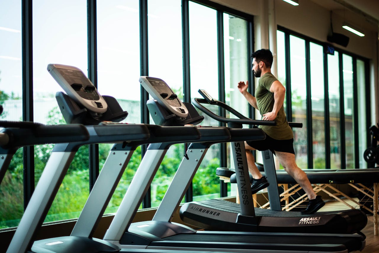journey Young man workouts on treadmill in modern gym with large windows and natural light.